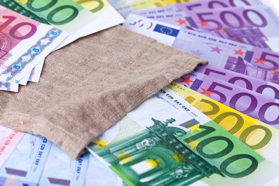 Ein hellblauer Geschenkgutschein im Wert von 25 Euro liegt neben einem Sparschwein und ein paar Münzen auf einem Holztisch.