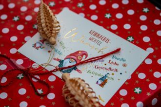 Ein goldener Geschenkgutschein über 100 Euro, verziert mit Tannenzweigen und einer roten Schleife, symbolisiert stressfreies und sparsames Schenken zu Weihnachten.