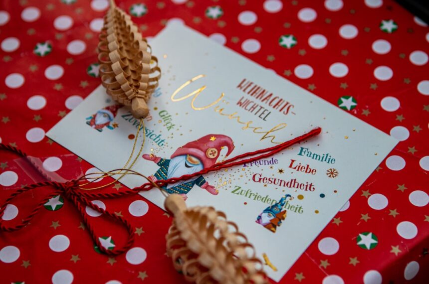Ein goldener Geschenkgutschein über 100 Euro, verziert mit Tannenzweigen und einer roten Schleife, symbolisiert stressfreies und sparsames Schenken zu Weihnachten.