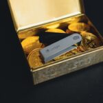 Ein Ledger Nano Gen 5 Hardware-Wallet liegt in einem offenen Tresor, umgeben von digitalen Münzen und einem Sparschwein.
